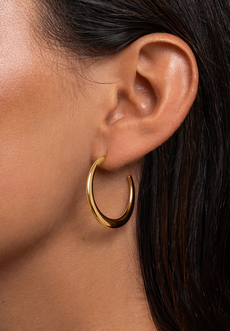 Boucle d'oreille en or avec une surface lisse et brillante. Forme circulaire avec une légère courbure, suspendue à l'oreille, mettant en avant un design contemporain.