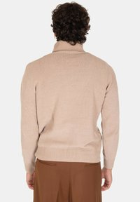 Maglione beige a coste con colletto alto, maniche lunghe e bordo aderente, realizzato in morbido tessuto a maglia. Visto da dietro.