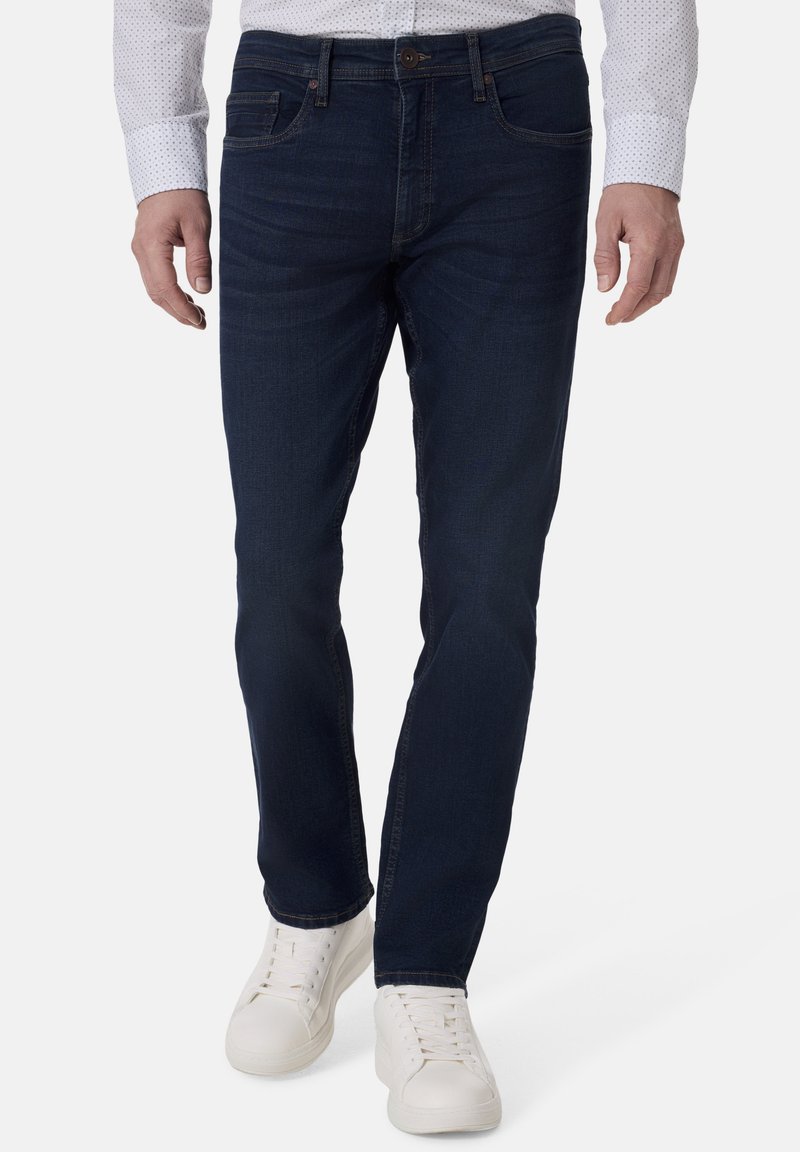 Dunkelblaue Jeans aus Denim mit geradem Schnitt, ausgestattet mit einem klassischen Fünf-Taschen-Design und dezenten Stickdetails. Kombiniert mit weißen Sneakers.