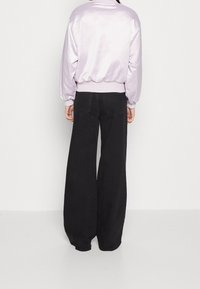 Lila satin bomberjacka med ribbad midja, kombinerad med svarta vida jeans med bakfickor och en slät yta.