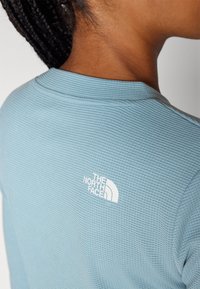 Un haut à manches longues de couleur bleu clair avec une surface texturée et un logo blanc de The North Face dans le haut du dos.