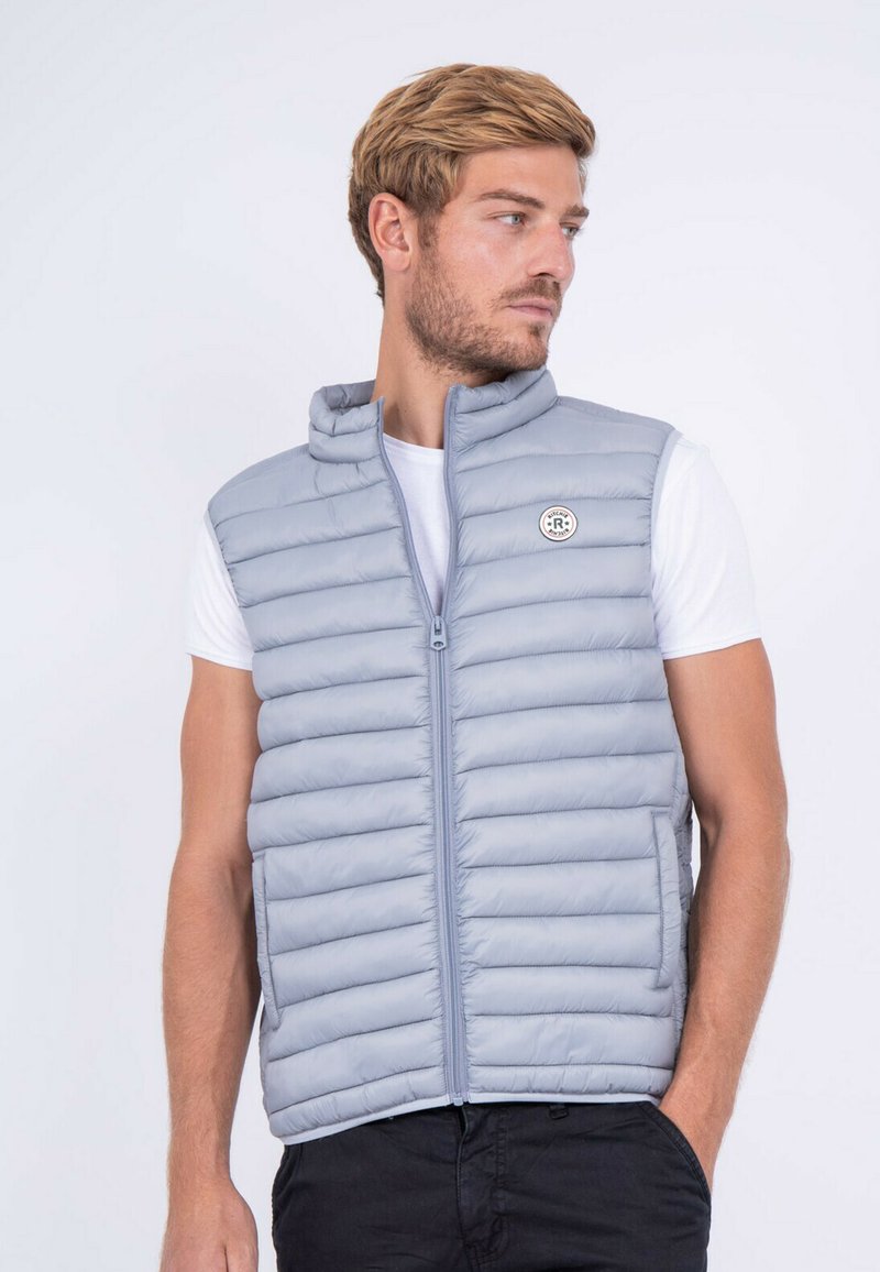 Gilet en duvet gris clair, sans manches avec un col montant, présentant des coutures horizontales, une fermeture éclair sur le devant et un patch logo sur la poitrine gauche.