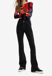 Long-sleeve top with a colorful floral pattern in red, blue, and beige; paired with fitted black flared jeans and black sneakers.