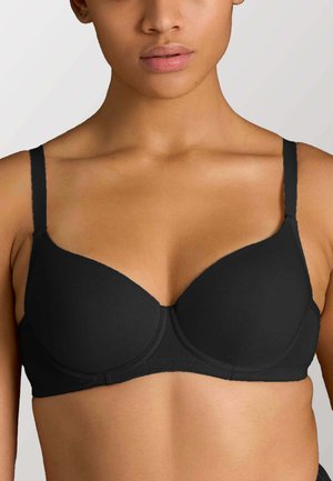 Primo piano di una persona che indossa un reggiseno nero semplice con ferretto e spalline regolabili su sfondo chiaro.