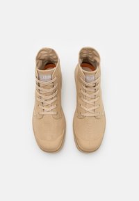Scarpe alta beige con tomaia in tela, punta in gomma e design con lacci. Le caratteristiche includono un collo imbottito e un'etichetta con il marchio sulla linguetta.