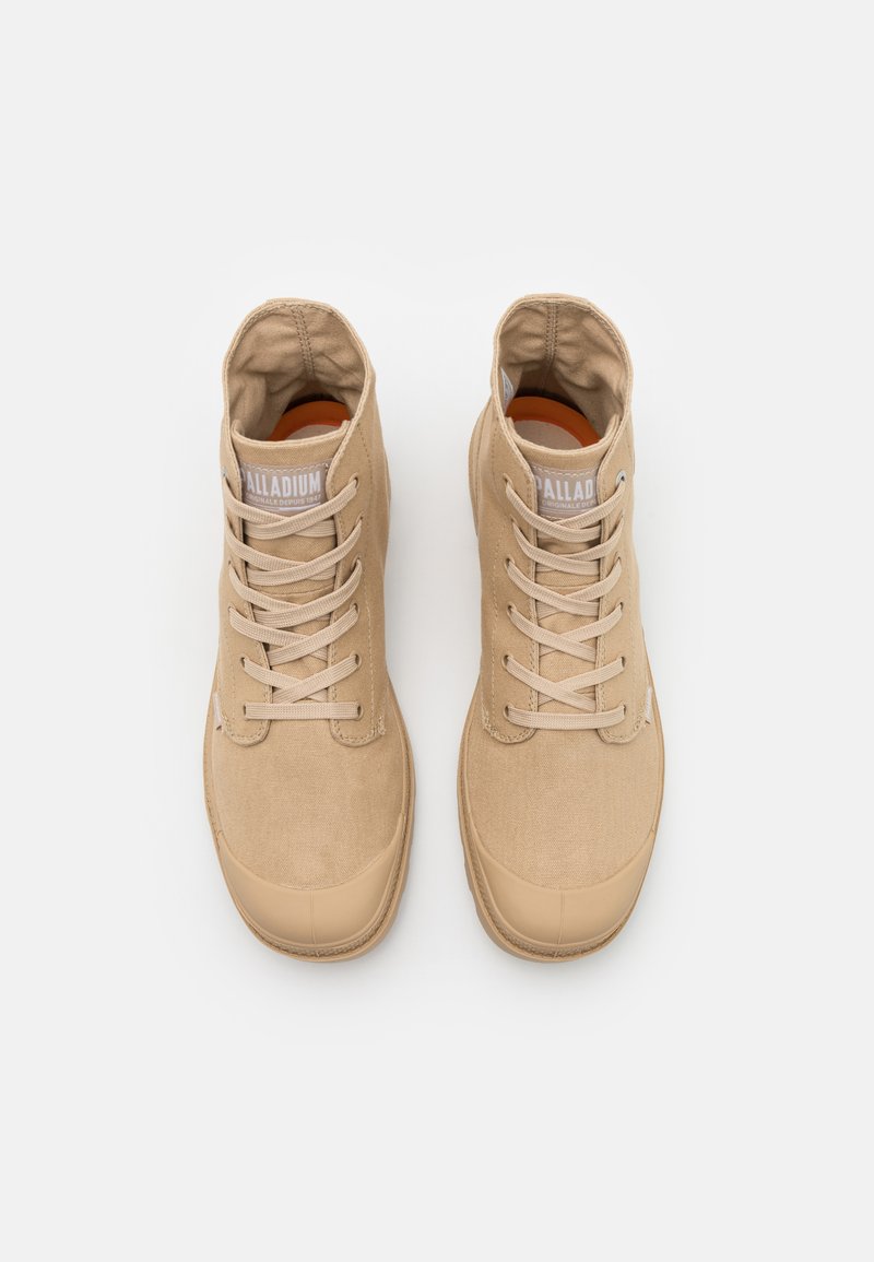Beżowe buty typu high-top z materiału canvas, gumowym czubkiem i sznurowanym zapięciem. Cechy obejmują wyściełany kołnierz oraz metkę z logo na języku.
