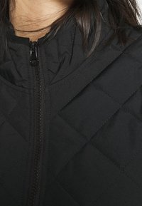 Sort quiltet jakke med høj krave og frontlynlås; blød tekstur med tydelig diamantmønster syning.