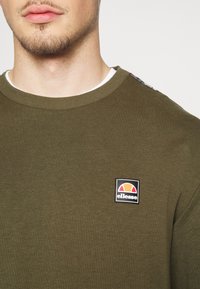 Felpa verde oliva in cotone, con collo a girocollo ribattuto, piccola toppa con logo sul petto e inserti decorati sulle spalle.