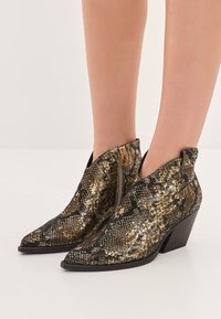 Bottines noires et dorées avec un motif serpent, bouts pointus et un petit talon empilé ; dotées d'une fermeture éclair sur le côté.
