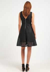 Robe noire avec un corsage ajusté, une jupe évasée au motif rayé, un dos en V et une fermeture éclair centrale au dos.