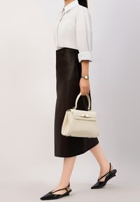 Camicia bianca con bottoni, gonna nera in pelle, ballerine nere con tacco a slingback e una piccola borsa crema con design strutturato e hardware dorato.