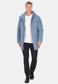 Világoskék téli dzseki kapucnival, elől cipzáros, oldalzsebekkel és enyhén párnázott kivitelben, fehér ing fölött viselve.