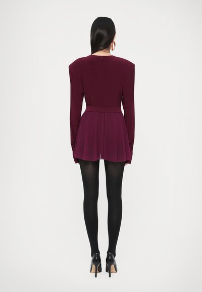 Burgundy dress with long sleeves, structured shoulders, pleated skirt, and a fitted waist. Worn with black tights and high-heeled shoes.