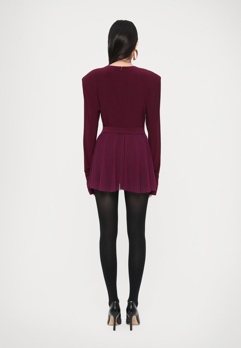 Vīnkrāsas kleita ar garām piedurknēm, strukturētām pleciem, plisētu svārku un pieguļošu vidukli. Valkāta ar melnām zeķubiksēm un augstpapēžu kurpēm.