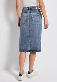 Jupe midi en denim bleu clair, avec une coupe droite, des poches arrière et un ourlet juste sous les genoux. Associée à des baskets blanches.