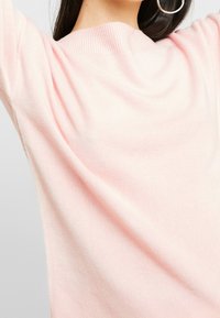 Jasnoróżowy sweter z dzianiny z okrągłym dekoltem i prążkowanymi wykończeniami. Materiał wydaje się miękki, o gładkiej teksturze i minimalnych detalach.