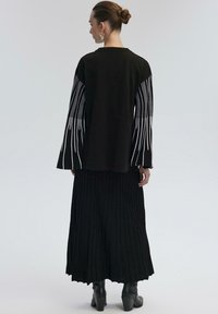 Black long-sleeve top with white vertical stripes on sleeves, paired with a black pleated skirt, worn with black heeled ankle boots.
