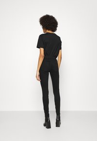 Camiseta negra combinada con jeans ajustados de cintura alta negros. Presenta un tejido suave, diseño ajustado y una silueta simple. Botas negras de tacón ancho.