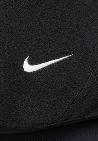 Black fabric featuring a prominent white Nike logo. The material appears soft and textured with visible stitching details.