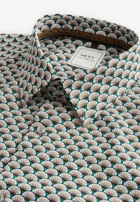 Tehát színes etiketttel rendelkező, galléros ing, amely teal, barna és fehér színű ventilátormintát tartalmaz. Gombokkal és a "NEXT TAILORING" felirattal készül.