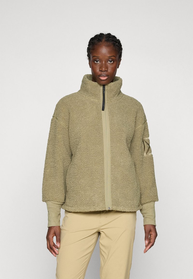 Giacca in fleece con zip di colore verde oliva, colletto alto, spalle scese e zip beige a contrasto. Tessuto spesso, morbido e strutturato.