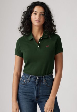 Dark green polo shirt with a collar and three buttons, featuring a red Levi’s logo on the left side. Worn with high-waisted blue jeans.