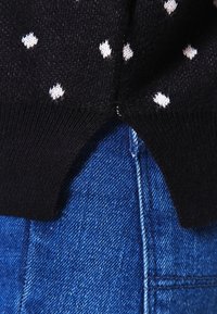 Czarny sweter w białe kropki, z ściągaczami na rękawach i rozciętym dołem, połączony z niebieskim denimm z widocznym przeszyciem.