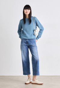 Sudadera de algodón azul, corte relajado, combinada con pantalones de mezclilla anchos de un azul claro. Zapatillas blancas con suelas beige y un pequeño bolso blanco.