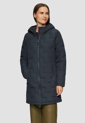 Donkere, gewatteerde jas met een capuchon, voorzien van een rits aan de voorkant, met een gestructureerd oppervlak en zijzakken. Draagt over groene broek.