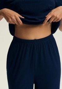 Granatowy, żeberkowy, dwuczęściowy zestaw odzieży domowej, składający się z krótkiego topu i spodni na elastycznej talii, charakteryzujący się miękką fakturą i luźnym krojem.