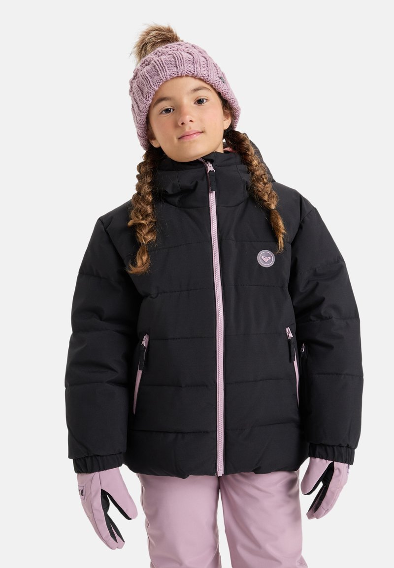 Jeune fille avec des tresses portant une doudoune noire, un bonnet tricoté rose avec un pompon, des gants roses et un pantalon rose, faisant face à l'avant.