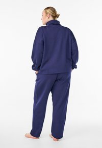 Navy blue sweatshirt with a high collar and oversized fit, paired with matching relaxed-fit pants, made from soft, textured fabric.
