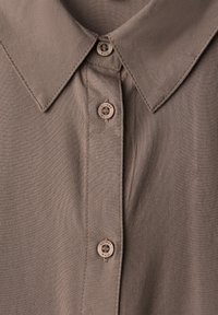 Camicia marrone con colletto, dal tessuto liscio, con bottoni marroni chiari e dettagli di cucitura lungo il pattino.