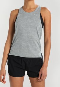 Top deportivo atlético gris claro con un patrón geométrico, combinado con pantalones cortos negros que presentan un logo. La tela es suave y transpirable.
