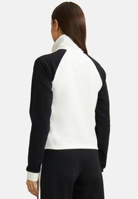 Sudadera en blanco y negro con cuello alto, mangas raglán y textura suave. Presenta colores contrastantes en la parte trasera y las mangas.