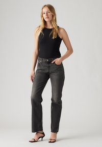 Zwarte tanktop gecombineerd met grijze rechte jeans. De jeans hebben een klassiek ontwerp met een vijf-pocket indeling en subtiele vervaging.