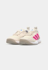 Beige joggesko med rosa detaljer og blå logo, med en teksturert mesh-overdel, polstret krage og gummisåle.
