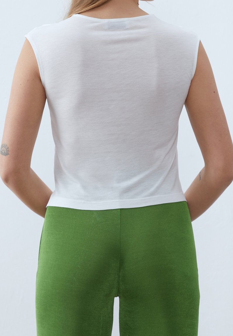 Vit bomulls-tanktopp med korta ärmar, med rund halsringning och en krokad fåll, tillsammans med gröna texturerade byxor.