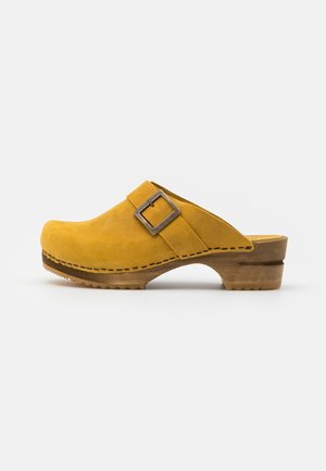 Sabot en daim jaune avec une semelle en bois, doté d'une bride à boucle argentée, surface lisse, bout rond et couture détaillée sur le côté.