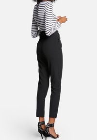 Svarta skräddarsydda byxor med smal passform, hög midja och ankellängd, kombinerade med en svart och vit randig långärmad topp och klackar med nitar.