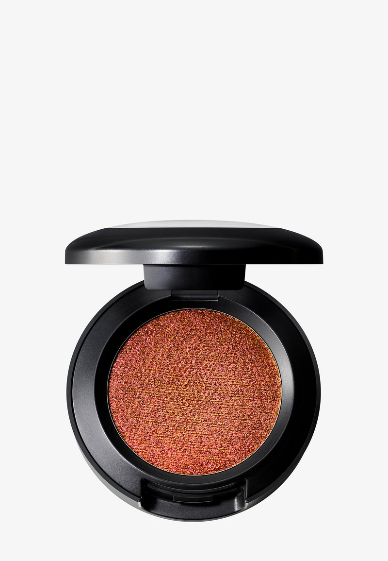 Compact de maquillage rond avec un couvercle noir laqué, contenant une poudre orange brûlée scintillante. La texture semble finement moulue avec une finition granuleuse.