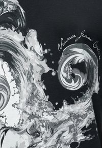 Μαύρο ύφασμα με αφηρημένο γκρι και λευκό σχέδιο στροβιλισμού νερού και καλλιγραφικό κείμενο που γράφει "Versace Jeans Couture."