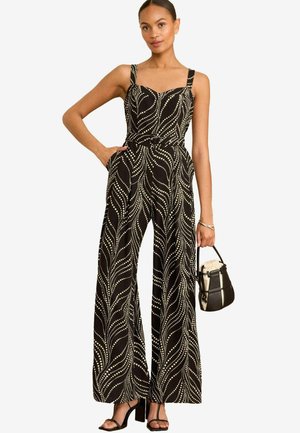 Zwarte jumpsuit met een getailleerde bovenkant, spaghettibandjes en wijde broekspijpen. Bevat een golvend wit patroon en een subtiele riem. Accessoires omvatten een kleine tas.
