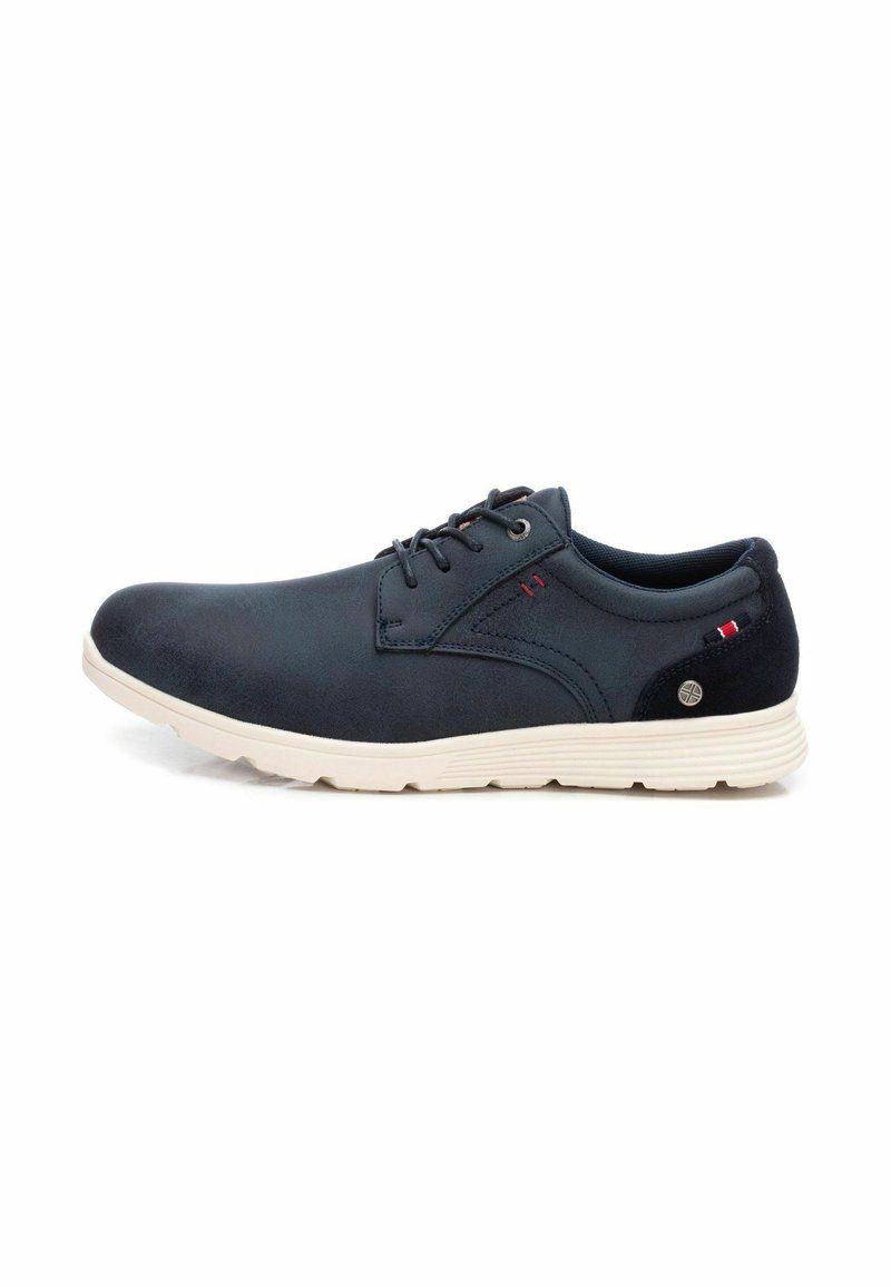 Zapatos de cordones azul marino hechos de materiales lisos y texturizados, con una suela blanca y un pequeño acento rojo y blanco en el lateral.