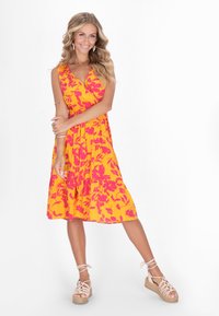 Rochie florală de culoare muștar, cu decolteu în V, bretele și fustă în straturi, decorată cu modele de flori roz. Asortată cu espadrile bej cu curele.