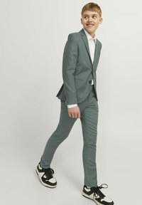 Completo grigio con design slim-fit, abbinato a una camicia bianca. I dettagli notevoli includono sneakers nere e bianche, che enfatizzano un contrasto casual.