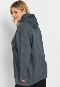 Sudadera de color gris oscuro con una tela texturizada, capucha amplia y hombros caídos. Presenta un corte relajado y bolsillos laterales para mayor comodidad.
