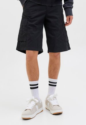 Shorts cargo noirs avec plusieurs poches, associés à des chaussettes blanches à rayures noires et des baskets gris clair. Ensemble de vêtements de sport décontractés.