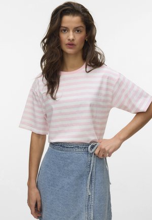 Vrouw met lang bruin haar die een roze-wit gestreept T-shirt en een hooggetailleerde spijkerrok draagt, en een strikje maakt in de tailleband van de rok.
