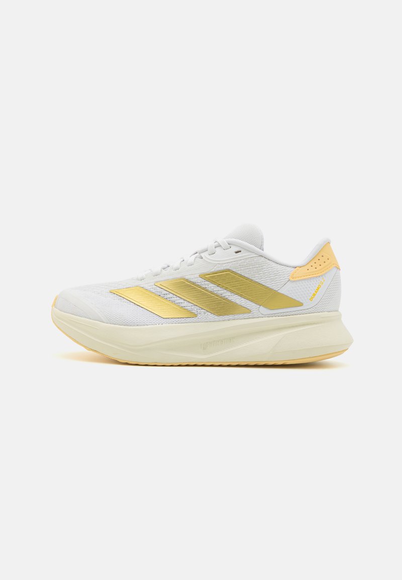 Zapatilla deportiva blanca con detalles dorados, parte superior de malla, suela ligera, diseño de tres rayas en el lateral y suela texturizada para mayor agarre.
